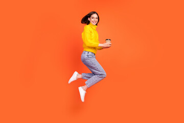 Fototapeta na wymiar Full length profile side photo of young woman happy positive smile jump takeaway coffee isolated over orange color background