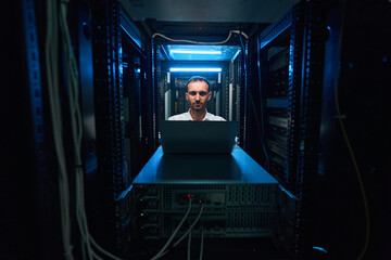 Data center worker sitting at laptop before server cabinet
