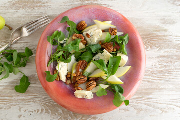 a plate of salad with arugula, pear, gorgonzola and nuts on a light table
