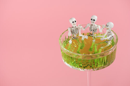 Three skeletons in a glass with a green drink on a pink background. Skeletons take a bath in a cocktail. Halloween party decorations