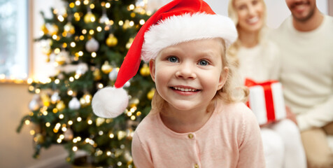 family, winter holidays and people concept - happy little girl and parents over christmas tree background