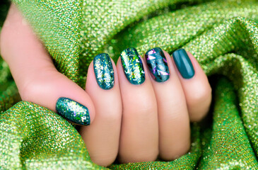 Festive manicure. Green shiny manicure on a shiny green background. Female fingers with green manicure.
