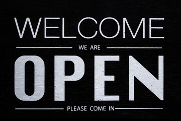 welcome we are open sign on black wooden board