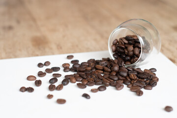 Roasted coffee beans in clear glass on white wooden background.