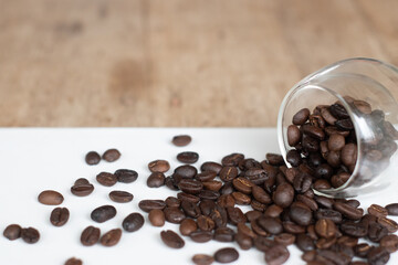 Roasted coffee beans in clear glass on white wooden background.