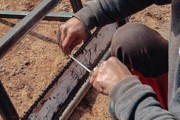 Closeup of lumberjack sharpening a chainsaw with file