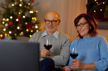 winter holidays, leisure and people concept - happy smiling senior couple with glasses of red wine watching tv at home in evening over christmas tree lights on background
