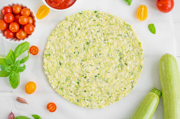 Preparation zucchini crust pizza with tomato sauce, mozzarella cheese, fresh tomatoes and basil on a white wooden background. Zucchini pizza Margarita. Healthy dish.