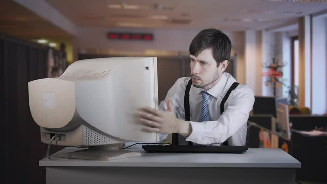 Angry man is beating old computer with hand in office.