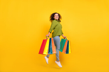 Photo of positive funny funky attractive beautiful stylish lady wear green shirt jumping holding colorful bargains isolated yellow color background