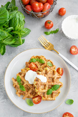 Homemade zucchini cheese waffles with sour cream and fresh basil on a plate on a gray concrete background. Vegetarian dish. Copy space.