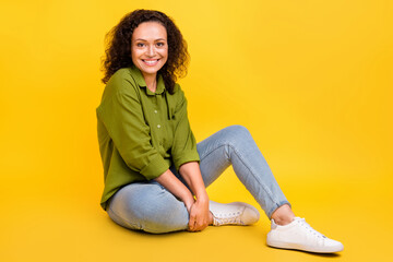 Fototapeta premium Photo of shiny pretty attractive lady wear green shirt smiling sitting floor having rest isolated yellow color background