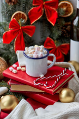 holidays, christmas and celebration concept - camp mug of whipped cream with marshmallow, candy canes, books and decorations at home