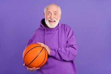 Portrait of attractive cheerful man holding orange ball leader pass isolated over bright violet purple color background