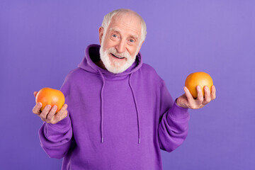Portrait of attractive cheerful grey-haired man holding in hands two grapefruits isolated over...