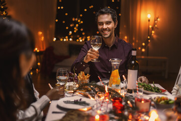 holidays and celebration concept - happy friends having christmas dinner at home and drinking red wine