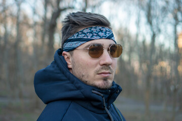 Fototapeta na wymiar Portrait of a young and stylish man in sunglasses and a bandana. Male model showing fashion. Style concept.
