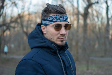 Portrait of a young and stylish man in sunglasses and a bandana. Male model showing fashion. Style concept.