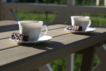 WHITE CUP ON SAUCER with sweets on the table in the morning sun