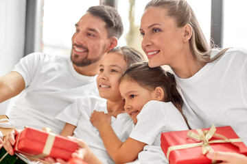 family, winter holidays and people concept - happy mother, father and two daughters in pajamas with christmas gifts in bed at home