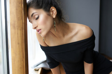 Fototapeta na wymiar beautiful woman in a black dress near the window posing fashion model