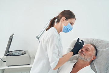 Fototapeta premium Doctor in medical mask making injection in man forehead