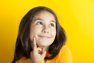 Portrait of a cute thoughtful child girl on yellow background in yellow t-short. People dream. Space for text.
