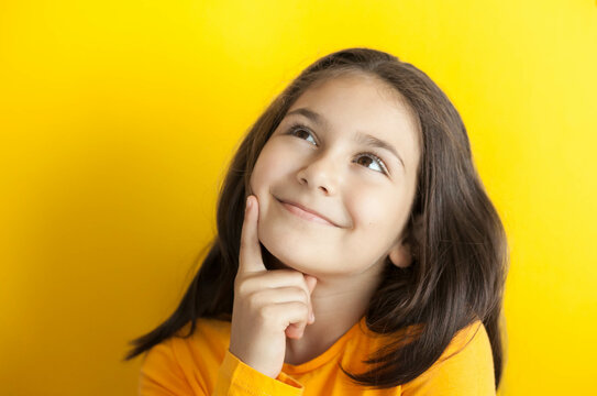 Portrait of a cute thoughtful child girl on yellow background in yellow t-short. People dream. Space for text.