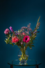 Fresh bouquet of flowers in a glass vase on a glass table with a dark blue background