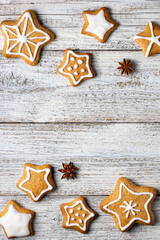 Border of Christmas gingerbreads in the shape of a star with patterns of glaze and spices on a white wooden background.