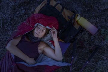 Woman mountaineer sleeping in a sleeping bag at nightfall in summertime using her backpack as a pillow