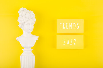 Trends 2022 written on rectangles on bright yellow background next to woman gypsum figure