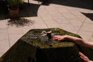 A child plays with water in a fountain on a hot day in the city. Contrasting photo with sharp shadows.