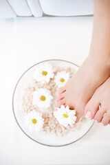 Obraz na płótnie Canvas Female feet with spa bowl, towel and flowers on white background