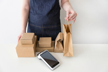 Woman entrepreneur wearing blue denim apron giving the kraft paper bag with an order to a customer