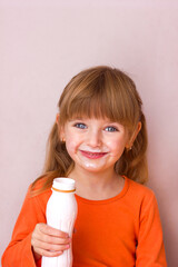 Portrait of a little beautiful girl with emotions on her face, her mouth stained with milk, holding a plastic bottle with a milk drink, yogurt or kefir, selective focus	