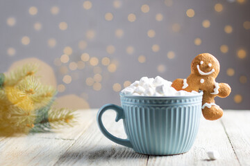 Obraz na płótnie Canvas A blue cup of winter hot drink with marshmallows and gingerbread man on a white wooden background with bokeh.