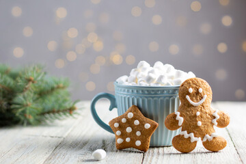 Obraz na płótnie Canvas A blue cup of winter hot drink with marshmallows and gingerbread cookies on a white wooden background with bokeh.