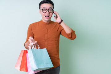 Young Asian man holding shopping bag on green background