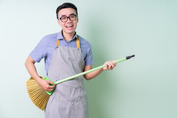 Young Asian man wearing apron posing on green background