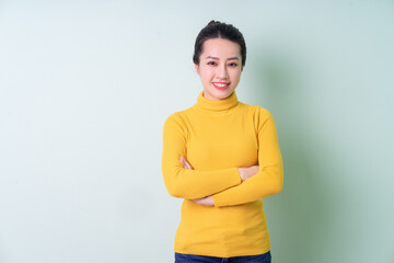 Beautiful young Asian woman wearing sweater on green background