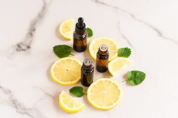 cosmetic bottles of dark glass with essential oils of lemon and lemon balm leaves on a marble table.
