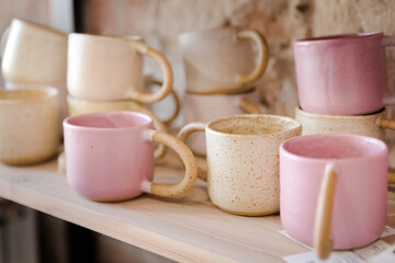 Handmade empty pink and yellow clay mugs composition on a wooden shelf with bricks in the background.
