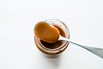 Homemade salted caramel in glass jar, white background, spoon with caramel