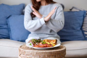 A woman making crossed arms hand sign to refuse food on the table for dieting and healthy eating...