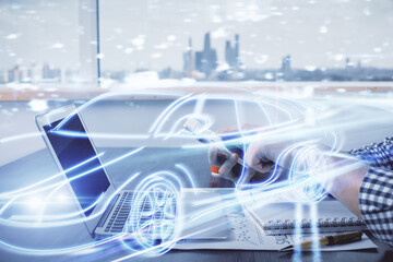 Double exposure of man's hands holding and using a digital device and automobile theme hologram drawing. Technology concept.