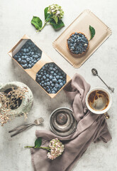 Flat lay with blueberries cake, coffee, wooden basket with fresh blueberries,dishcloth, water glass and flowers on white background. Cozy tea time with homemade pastry and hot drinks. Top view.
