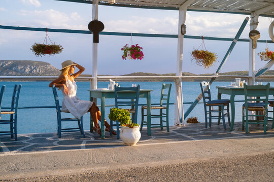 Young woman tourist in straw hat sitting at cafe at Ermioni marina, Greece