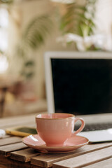 Laptop,pink cup and a smartphone on the wooden table.Indoor plants and flowers in the background.A modern and cozy workplace.Business,e-learning, freelance, technology concept.Copy space for text.