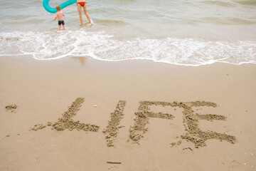 The word LIFE is written on the beach sand. Happy family among the turquoise waves.